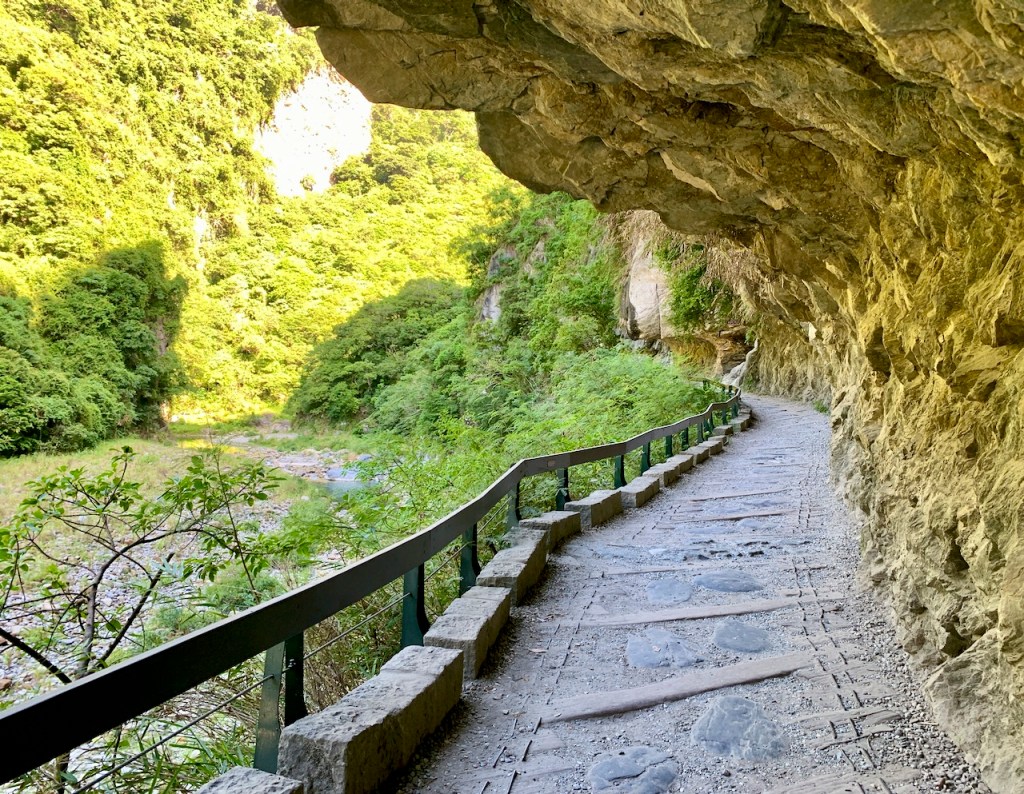 Rock paved Shakadang trail with cliff overhang alongside a low-level river